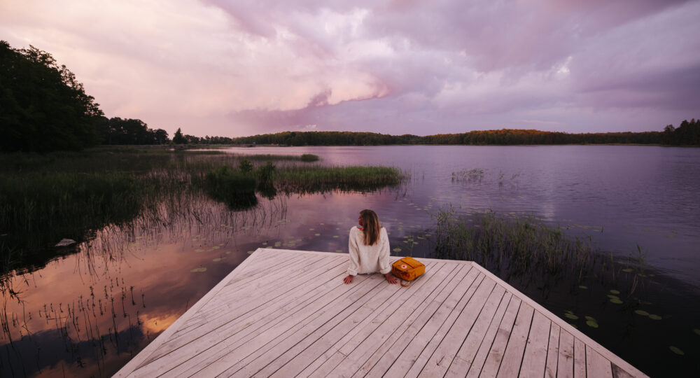 Kvinna sitter på brygga i solnedgång. Foto: Alexander Hall/Destination Småland