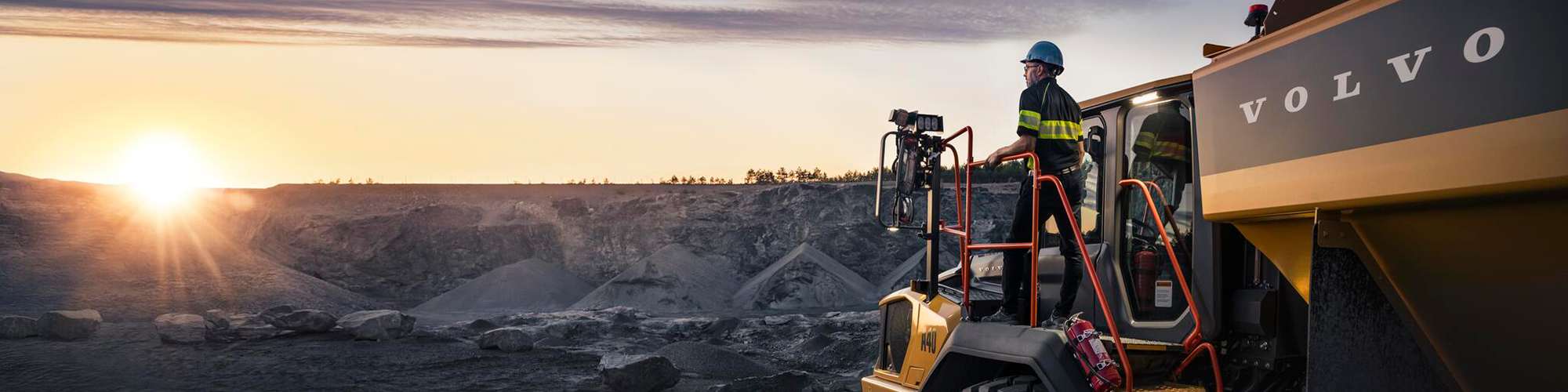 Volvo-dumper och en förare i solnedgång.